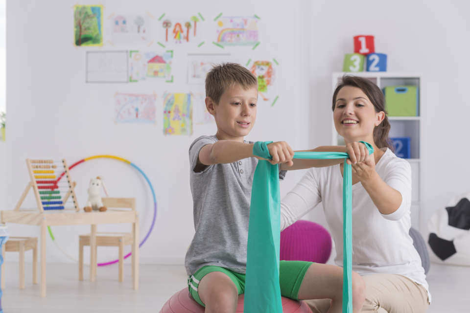 Physiotherapist and boy sitting on a gym ball