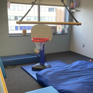 Pediatric therapy room at Good Beginnings Therapy in Falls Church, VA, featuring a suspended swing, soft mats, and a child-sized basketball hoop used for sensory integration, coordination, and motor skill activities.