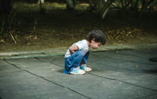 Young child in a deep squat position outdoors, demonstrating physical posture relevant to pediatric bowel and bladder therapy.